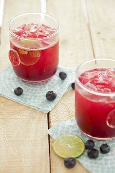 two glasses filled with blueberries and lemonade on top of napkins next to each other