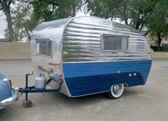 an old blue and silver trailer parked in a parking lot next to a classic car