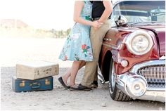 a man and woman leaning on the hood of a car next to an old suitcase