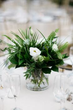 a vase filled with white flowers sitting on top of a table next to wine glasses