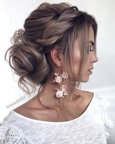 a woman with her hair in a low bun, wearing earrings and a white top