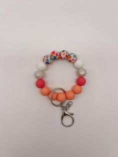 an orange, white and pink beaded bracelet on a keychain with a metal hook