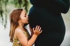 a pregnant woman kissing her child's belly in front of a body of water