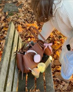 a woman sitting on a wooden bench next to a brown purse and some yellow cups