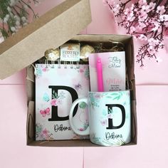 an open box with two mugs and some candy in it on a pink surface