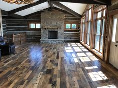 an empty living room with wood floors and stone fire place in the center, surrounded by large windows