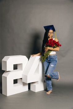 a woman in graduation cap and jeans holding flowers next to the letters that spell 24