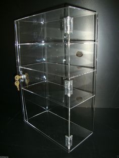 a clear display case with several drawers and keys on the bottom shelf, in front of a black background