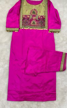 a bright pink dress with gold trimmings on the neck and sleeves, sitting on a