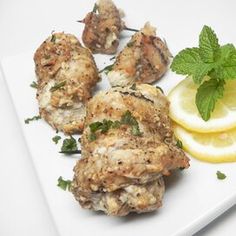 chicken with lemon and mint garnish on a white plate next to a slice of lemon