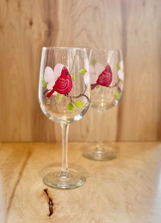 two wine glasses sitting on top of a wooden table next to each other with red birds painted on them