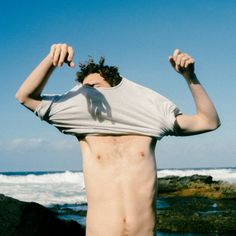 a man standing on top of a beach next to the ocean holding his hands up