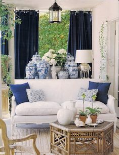 a living room filled with white furniture and blue and white vases on the windowsill