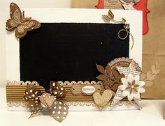 an altered photo frame with paper flowers and butterflies on the front, sitting on a table next to a brown bag