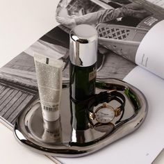 a silver tray with two bottles and a watch on it next to an open magazine