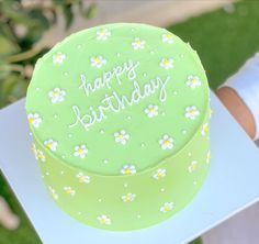 a green birthday cake with daisies and the words happy birthday on it is being held by a person