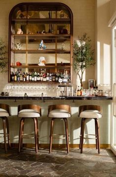 three stools sit at the bar in front of an open cabinet with bottles on it