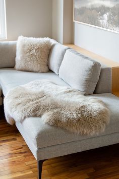 a couch with white fur on it in front of a window and wood flooring