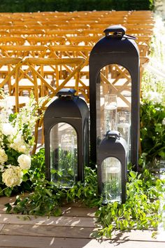 two black lanterns sitting on top of a wooden floor next to white flowers and greenery