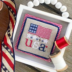 an american flag cross - stitch pattern in a white frame next to some spools of thread