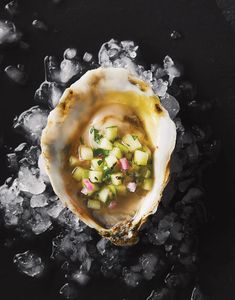 an open oyster with cucumber and other vegetables on top of ice cubes