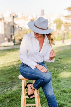 a woman sitting on top of a wooden stool wearing a white shirt and cowboy hat