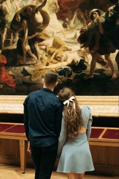 a man and woman are standing in front of a painting with their back to the camera