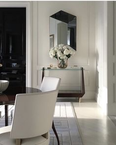 a dining room table with white chairs and flowers in a vase on the sideboard