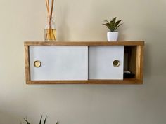 a wooden shelf with two white drawers and some plants on top of it next to a potted plant