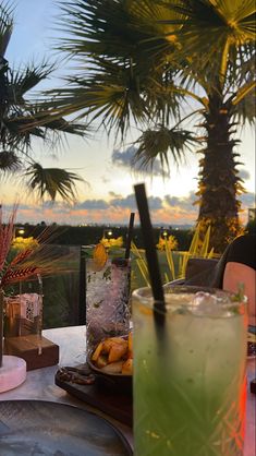 two drinks are sitting on a table with palm trees in the background