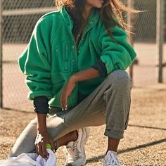 a woman sitting on the ground with tennis racket in her hand and wearing a green jacket