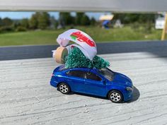 a blue toy car with a christmas tree on top of it's roof, parked in front of a building