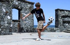 a young man kicking a soccer ball on top of a cement field next to the ocean