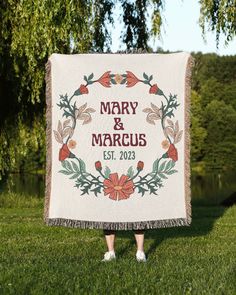 a woman standing in the grass holding up a wedding blanket that says mary and marcus