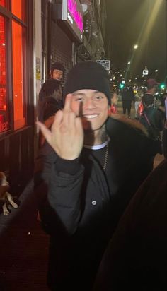 a man standing in front of a building giving the peace sign with his hand while wearing a black hat