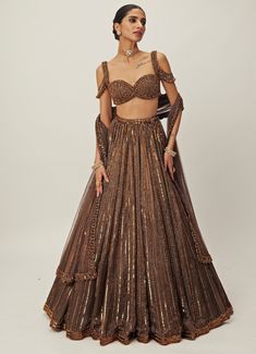 Elevate your wardrobe with this breathtaking Copper Crystal Linear Embroidered Organza Lehenga Set, a masterpiece of intricate craftsmanship perfect for making a bold style statement. Made from luxurious organza fabric, the copper lehenga features exquisite linear embroidery adorned with sequins, cutdana, and crystal embellishments, adding a radiant sparkle to the flowing design. Paired with a jewelled georgette blouse, the lehenga set offers a modern twist with its chic cut and crystal embroidery. The rich copper hue is beautifully complemented by the matching tulle dupatta, intricately detailed with shimmering accents. Ideal for weddings, receptions, or cocktail. The off shoulder tassels details can be added for an additional GBP 45. Composition : Lehenga - Organza, Dupatta - Soft Net an Copper Lehenga, Linear Embroidery, Shoulder Tassels, Indian Lengha, Vani Vats, Organza Lehenga, Crystal Embroidery, Weddings Receptions, Copper Crystal