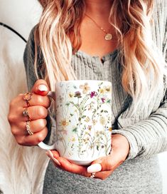 a woman holding a coffee mug with flowers on it