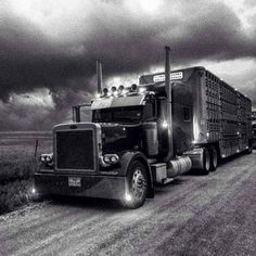 a black and white photo of a semi truck on a road with storm clouds in the background