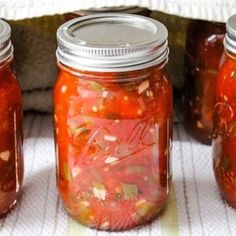 three jars filled with pickled vegetables sitting on top of a cloth covered tablecloth