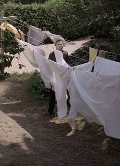 clothes hanging out to dry on a line in front of bushes and trees, with a person standing next to them