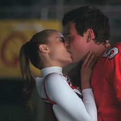 a man and woman kissing each other in front of a football uniform on the field