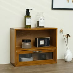 a wooden shelf with some bottles and soaps on it next to a white vase