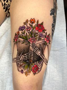 a tattoo on the leg of a woman with flowers and two hands holding each other