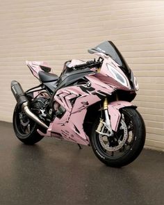 a pink motorcycle parked in front of a brick wall