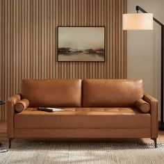 a brown leather couch sitting on top of a rug next to a lamp and painting