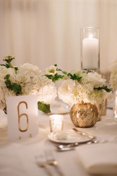 the table is set with white flowers and gold vases, candles and napkins