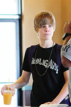 a young man standing next to a table with a drink in it's hand