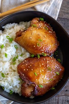 two pieces of chicken and rice in a bowl with chopsticks on the side