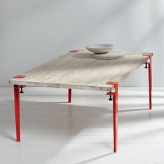 a wooden table with two red legs and a white bowl on top, against a wall