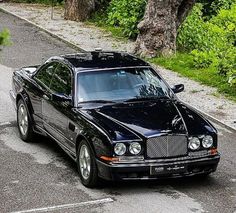 a black car parked on the side of a road next to a tree and bushes